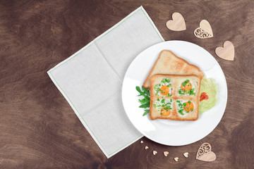 Scrambled fried eggs and bread in the shape of a heart with hot toasts and fresh vegetables served on a wooden table. Romantic breakfast on Valentine's Day or Mother's Day