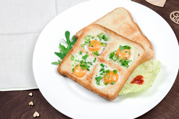 Scrambled fried eggs and bread in the shape of a heart with hot toasts and fresh vegetables served on a wooden table. Romantic breakfast on Valentine's Day or Mother's Day. Top view, closeup