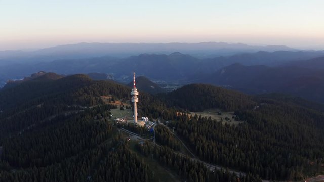 Snezhanka Tower, Pamporovo, Bulgaria. Aerial view from drone slide forward on tower structure high in mountains, above dense pine forest at sunset in summer evening. Nature