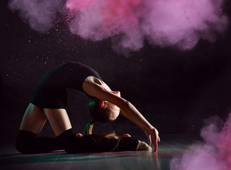 Young girl gymnast in black sport body and special footwear making gymnastic pose over dark...