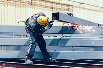 Worker grinding a steel profile in factory.