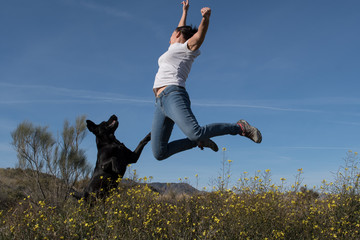 Labrador dog with middle-aged woman jumping together with joy in nature.
