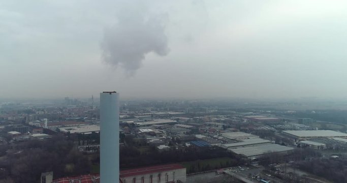 Steaming chimney with industrial area in the background. Polluted air on winter day.