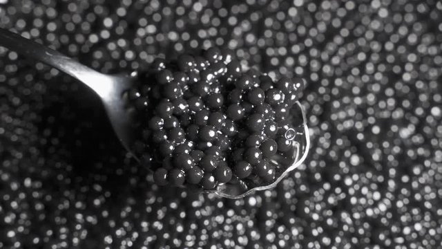 Spoon with black caviar on a background of rotating black caviar