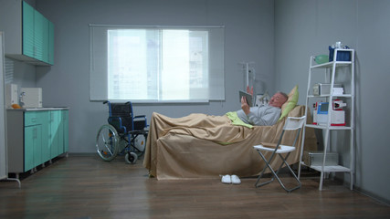 Man lie on the bed in the hospital and talk with someone on tablet