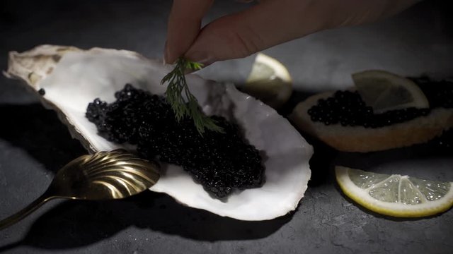 Black caviar is served on a plate in the form of a real shell with mother of pearl. Woman adds greens for decoration