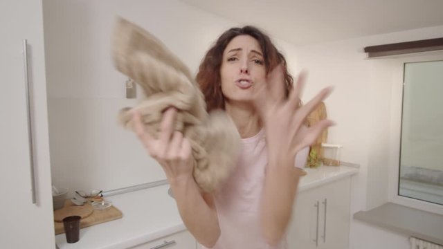 POV waist-up shot of hysterical young Caucasian woman standing in kitchen by sink holding towel, tearfully complaining and reproaching, crying while holding head in hands and screaming