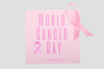 Pink ribbon and paper sheet with text WORLD CANCER DAY on white background