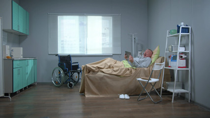 Man lie on the bed in the hospital, watch on tablet and react emotionally 