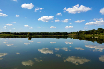 reflection of the sky in water, a beautiful background with blurry reflection of green trees and white clouds.