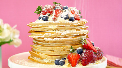 Shrove Pancake Tuesday, last day before Lent, stack of pancakes cake prepared with layers of whipped cream and fresh berries against modern pink background. Close up.