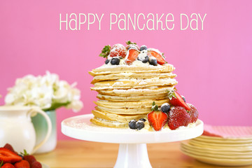 Shrove Pancake Tuesday, last day before Lent, stack of pancakes cake prepared with layers of whipped cream and fresh berries against modern pink background. Happy Pancake Day greeting text message.