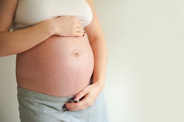 Pregnant cares for her stomach on a gray background close-up and copy space.