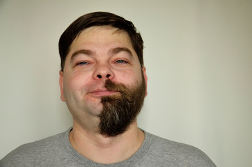 The bearded man smiles, half of his face shaved off. Portrait of a man.