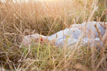 Young pregnant woman lied on the dried grass against the sunset. wiman holding the belly.  girl wearing fashion knitted sweater. the girl  care to be maternity