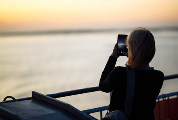 The girl tourist photographs the sunset on the phone by the lake in Norway. Silhouette at sunset of young woman.Travelling, lifestyle, adventure, wild nature concept.