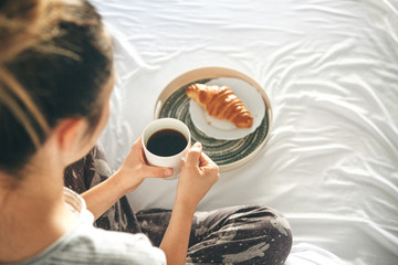 Girl drinks morning delicious coffee with a croissant in bed.