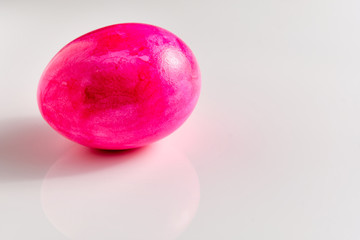 Bright pink easter egg with some first fine little cracks in the eggshell lying on white ground with copy space