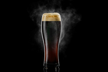 Cold pilsner beer glass with black porter beer inside covered with drops and froth evaporating on black background. - obrazy, fototapety, plakaty