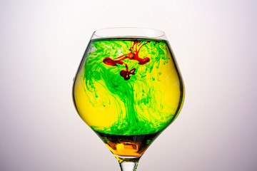 Red , green and yellow food coloring diffuse in water inside glass , with gradient background