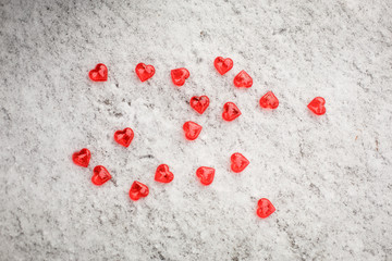 Red glass hearts are scattered on the snow. Symbols for Valentine's day, background with snow texture and hearts