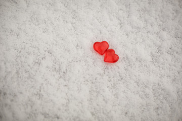 Two red glass hearts on the snow. Symbols for Valentine's day, background with snow texture and hearts