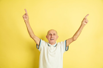 Pointing up. Caucasian senior man's portrait isolated on yellow studio background. Beautiful male emotional model. Concept of human emotions, facial expression, sales, wellbeing, ad. Copyspace.