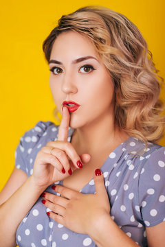 Girl with red lips and a dress in peas on a yellow background. Pin-up portraits. Shows a gesture of silence