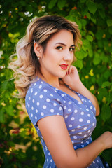 Girl with red lips and a dress in peas on a background of trees in the park. Pin-up model on a background of red apples.