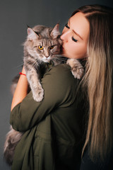 The girl holds a fluffy cat in her hands. Model on a gray background, studio photo. Love between a man and a pet