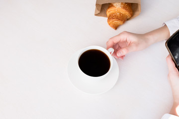 White cup with coffee in hand on a white background and fresh croissant