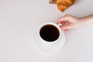 White cup with coffee in hand on a white background and fresh croissant