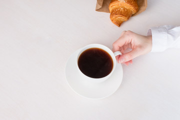 White cup with coffee in hand on a white background and fresh croissant