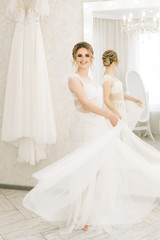Fototapeta premium Portrait of a beautiful young bride in a bright room in a romantic atmosphere. Bride in a negligee with wedding hair and makeup