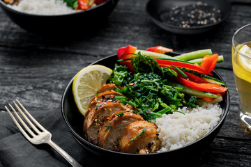 Wholesome meal made of teriyaki chicken fillet, fresh cucumber, red bell pepper, stew cabbage and basmati rice. Delicious Couple buddha bowls with lemonade on a black table.