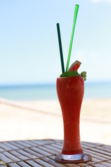 Watermelon smoothie served in a tall glass and sea view.