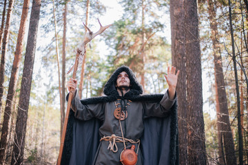 A man with a beard and a mustache in a robe and coat with a staff in his hand. A magician, a shaman...