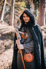 A man with a beard and a mustache in a robe and coat with a staff in his hand. A magician, a shaman...