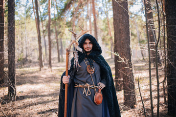 A man with a beard and a mustache in a robe and coat with a staff in his hand. A magician, a shaman...