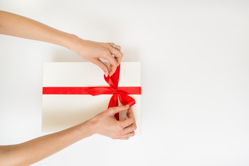 Female hands holding a gift box white with a red ribbon