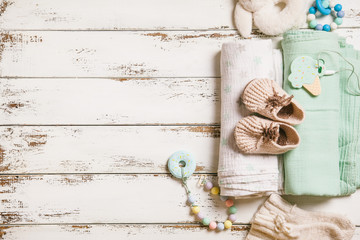 Newborn baby swaddling clothes, bootees, teethers and toy on white wooden background with copy space. Baby fashion concept.