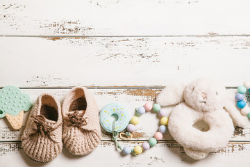 Newborn baby bootees, teethers and toy on white wooden background with copy space. Baby fashion concept.