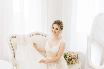 Portrait of a beautiful young bride in a bright room in a romantic atmosphere. Bride in a negligee with a wedding dress