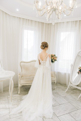 Fototapeta premium Portrait of a beautiful young bride in a bright room in a romantic atmosphere. Bride with a bouquet of flowers