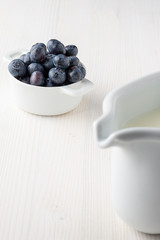 Close-up of unfocused white milkmaid, blueberries in bowl in the background focused, on white wood in vertical with copy space
