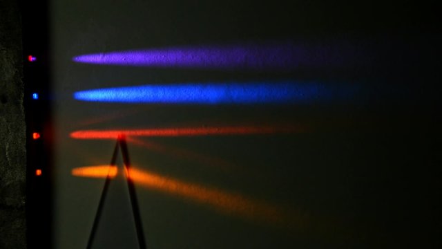 Four different light beams are refracted in two triangular prisms, first a 30 degrees refract the beams downwards, then a 45 degrees prism refract even more the other way, seen on a dark background.