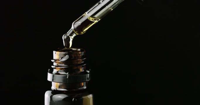 CBD Hemp oil, Hand holding droplet of Cannabis oil against black background. Alternative Medicine. 4k slow motion