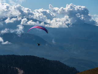 Paraglider flies above the clouds over the mountains and over the forest