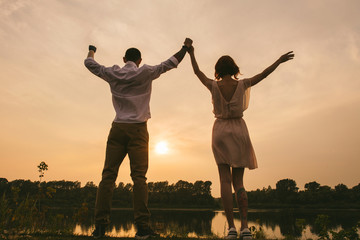Couple standing on a river shore, celebrating a beautiful sunset taking place.