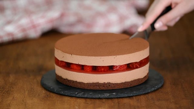 Woman's hands cut the delicious chocolate mousse cake with raspberries jelly.